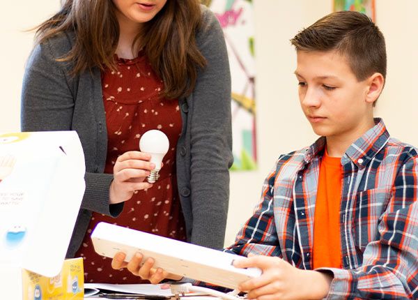 teacher holding a lightbulb and student holding an outlet extension