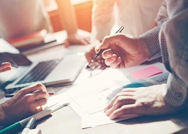 group of people standing around a table with pens and paper and a computer