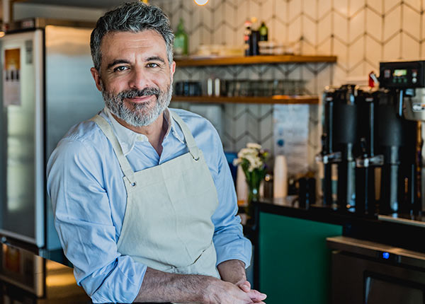 man in apron leaning on restaurant bar