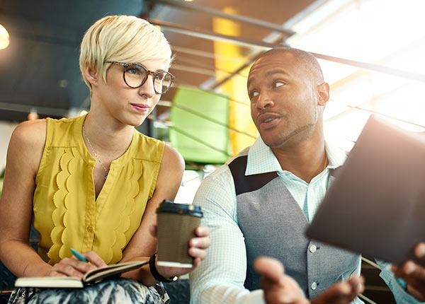 man and woman discussing something on an ipad and drinking coffee